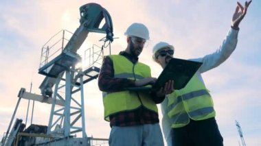 Erkek mühendis yağ pompaları yakınındaki bir petrol sahası üzerinde çalışıyor.