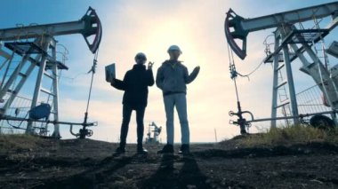 İnsanlar petrol derricks günbatımı bir arka plan üzerinde yakın durmak, yakın çekim.