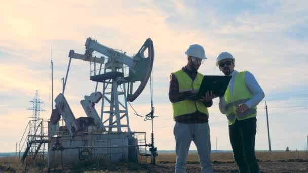 Deux travailleurs debout sur un champ pétrolifère près de pompes à pétrole . — Video