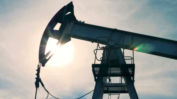 Olie derrick werkt op de achtergrond van een zon, close-up. Metalen toren pompen olie op een olieveld. — Stockvideo