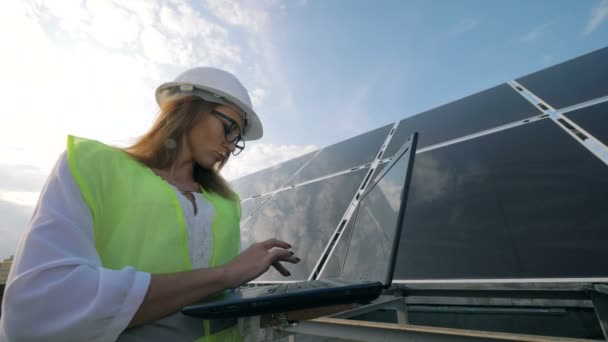 Belle femme utilise son ordinateur portable tout en étant près d'une construction solaire — Video