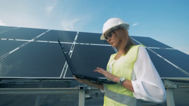 Bauarbeiterin läuft mit Computer an einem Solarpanel entlang — Stockvideo