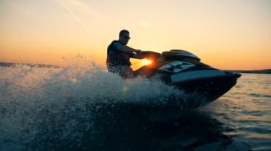 Bir adam bir jet-ski kıyı şeridi boyunca günbatımı sırasında biniyor