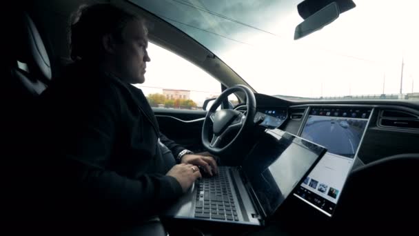Il conducente guida un'auto con pilota automatico mentre lavora con un computer portatile, da vicino . — Video Stock