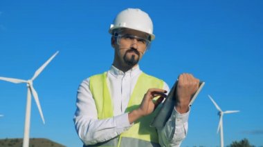 Erkek işçi bir tablet türbini kuleleri yanında dururken faaliyet göstermektedir. 4k