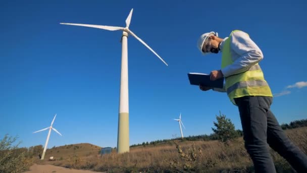 Mannelijke technicus met een Klembord is het observeren van verschillende windmolens. Schone, eco-vriendelijke energieconcept. — Stockvideo