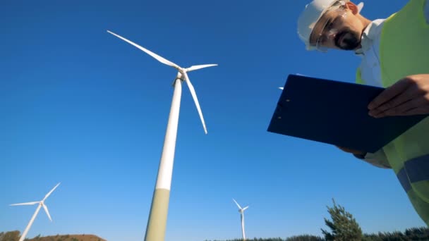 Rotierende Windkraftanlagen und ein männlicher Spezialist in ihrer Nähe. sauberes, umweltfreundliches Energiekonzept. — Stockvideo