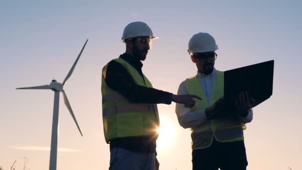 Dois engenheiros estão conversando ao lado de um aeromotor durante o pôr do sol. Energia alternativa renovável, conceito favorável ao ambiente . — Vídeo de Stock