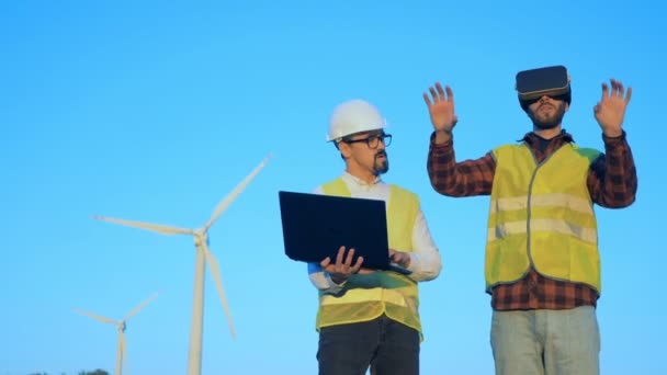 Energetikai mérnök, a virtuális valóság szemüveg van lét navigált egy másik szakértője, szélmalom közelében. — Stock videók