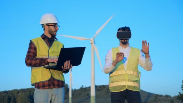 Dois técnicos estão controlando turbinas eólicas com um laptop e óculos virtuais. Conceito de energia limpa e ecológica . — Vídeo de Stock