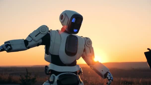 Engineer is manipulating a robot by his laptop in sunset landscape — Stock Video