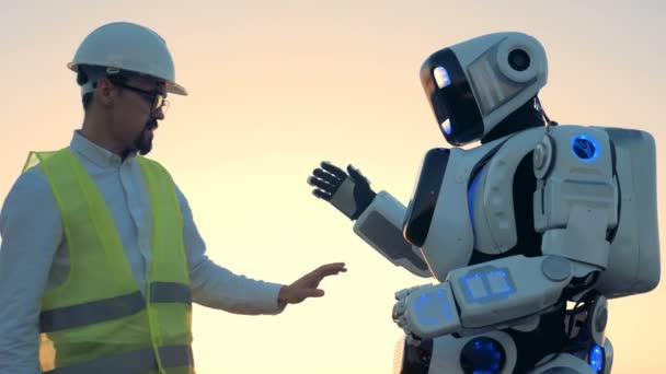 Robots de apariencia humana están siendo regulados por un ingeniero en un hardhat — Vídeos de Stock