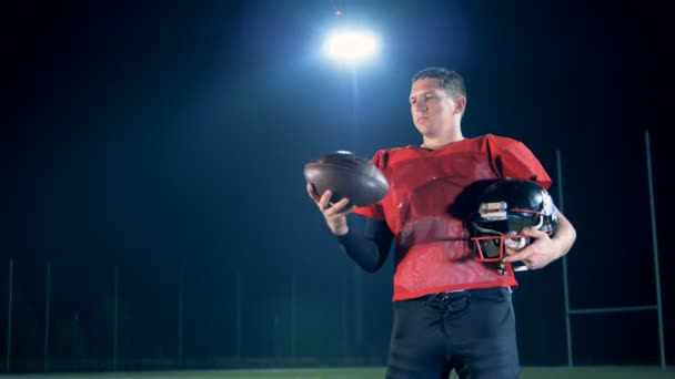 Αρσενικό ποδοσφαιριστής Αμερικανός αθλητής παίζει με μια μπάλα ενώ στέκεται στο στάδιο — Αρχείο Βίντεο