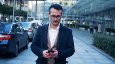 Yetişkin bir adam onun smartphone tarafından yakındaki bir şehir bina yürürken resimleri alıyor.