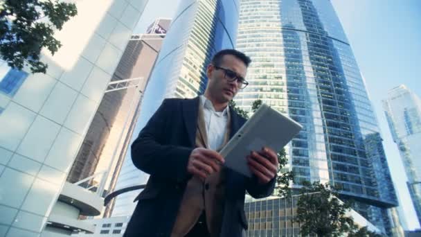 Επιχειρηματίας αρσενικό, διευθυντής στέκεται κοντά σε ουρανοξύστες με ένα tablet. — Αρχείο Βίντεο