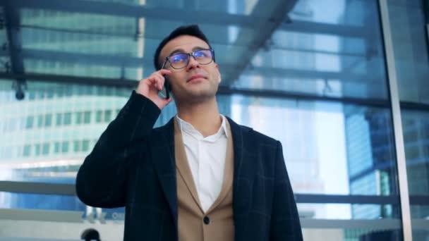 Businessman is smiling and talking on the phone while standing near a business center. Red epic cinema camera shot. — Stock Video