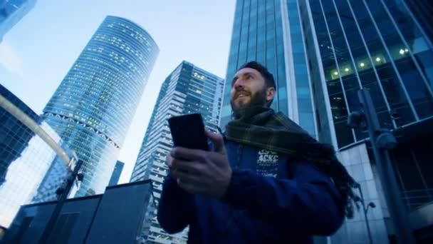 Турист управляет своим смартфоном, находясь рядом с небоскребами. Эпическая кинокамера . — стоковое видео