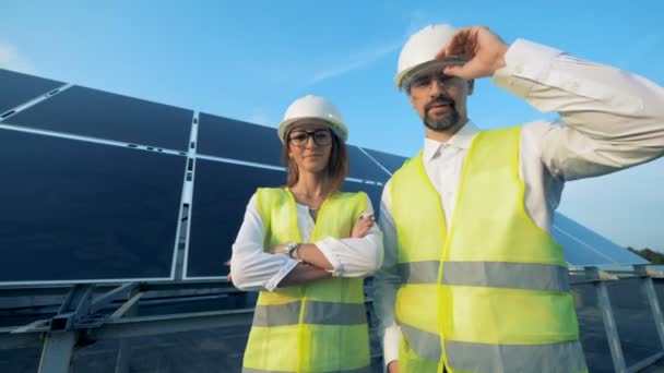 Engenheiros de energia sorridentes estão de pé ao lado de uma bateria solar e olhando para a câmera. Conceito de energia verde . — Vídeo de Stock