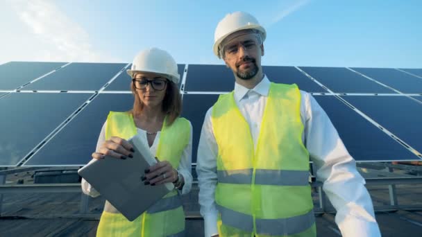 Instalación solar y dos inspectores de pie frente a ella y sonriendo mirando a la cámara . — Vídeo de stock