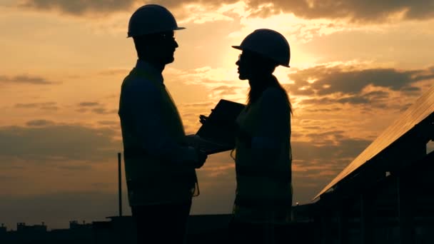 Два силуети інженерів розмовляють на даху під час заходу сонця — стокове відео