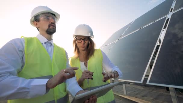 Ein weiblicher und ein männlicher Solarinspektor diskutieren in der Nähe eines Solarmoduls. Grünes Energiekonzept. — Stockvideo