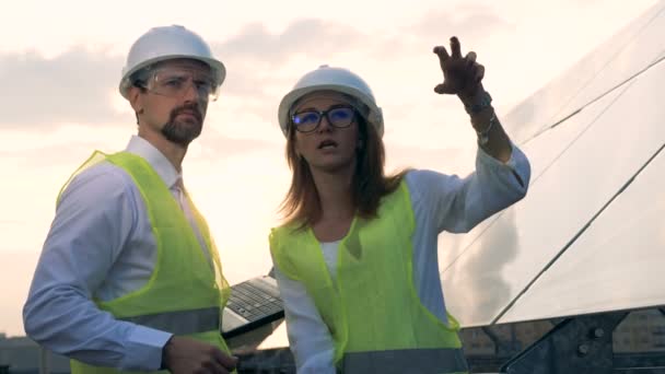一名男性和一名女性工程师讨论太阳能站在太阳能电池板附近。太阳能概念. — 图库视频影像