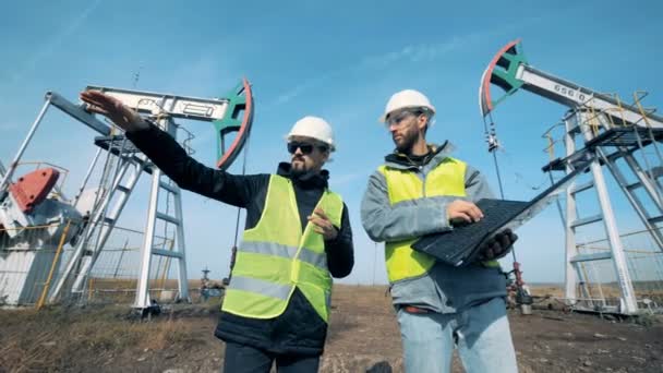 Oil-derricks un dos inspectores masculinos teniendo una discusión cerca de ellos. Bombas de aceite de trabajo, plataformas de aceite sobre un fondo . — Vídeos de Stock