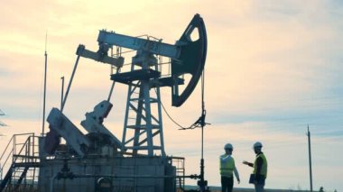 İki erkek işçiler petrol derrick, petrol sondaj platformu, yağ pompası yakınındaki tartışma süreci. Çalışma yağ pompaları, bir arka plan üzerinde petrol kuyularında.