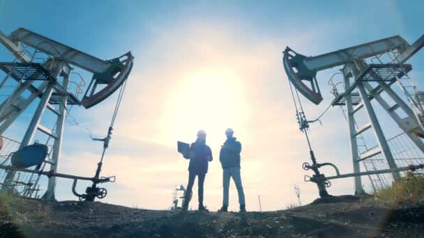 Deux travailleurs masculins rétro-éclairés se tiennent entre deux grues à huile — Video