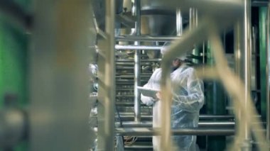 Onun tableti boru hatları tarafından çevrili bir fabrika tesis erkek işçi çalışıyor