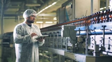 İşçi tablet kullanarak bir konveyör şişe denetler.