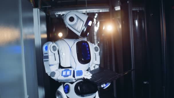 Um robô trabalha em um data center. Droid fica com um laptop nas mãos em uma sala de servidores . — Vídeo de Stock
