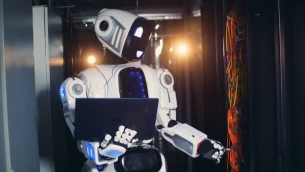 Un cyborg blanco escribe en un portátil en una sala de servidores. Robot se encuentra en una habitación, comprobando el equipo del servidor . — Vídeos de Stock