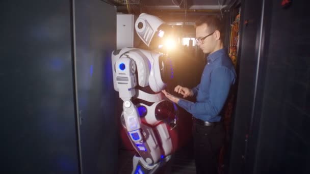 Τύποι μηχανικός σε μια οθόνη ρομπότ. Ένας προγραμματιστής και ένα droid στέκονται σε ένα δωμάτιο διακομιστή, ετοιμάζεται για το έργο. — Αρχείο Βίντεο
