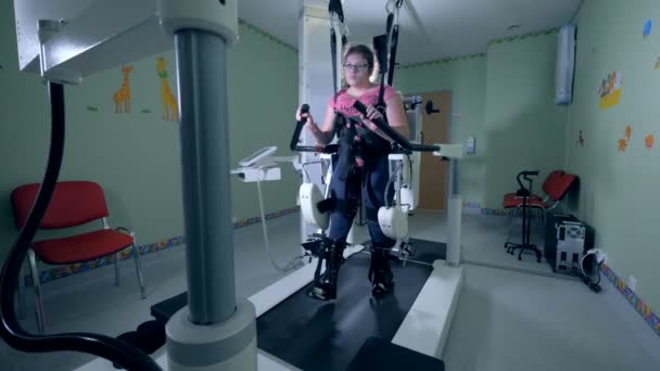 リハビリテーション機器の助けを借りて歩行練習を通して身体障害者の若い女の子が起こっています。. — ストック動画