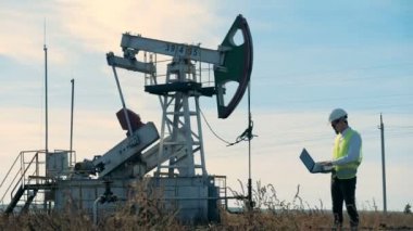 Bir kişi ile dizüstü çalışan petrol derrick yakınındaki elinde duruyor.