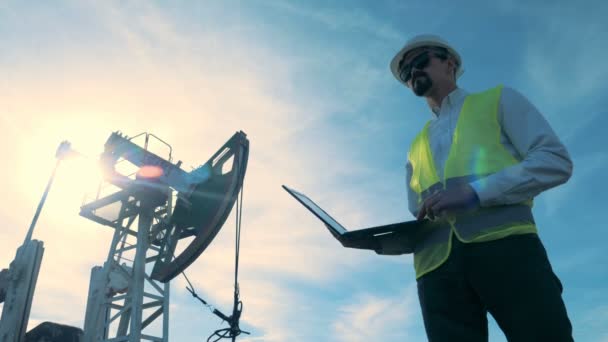 Un ingeniero escribe en un ordenador portátil en un fondo derrick aceite, de cerca . — Vídeo de stock