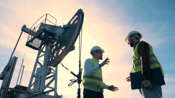 Gli operai del campo petrolifero parlano su uno sfondo della torre petrolifera, vista dal basso . — Video Stock