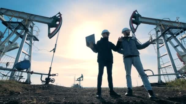 Ingenieros de pie en un campo petrolífero sobre un fondo de sol, vista inferior . — Vídeo de stock