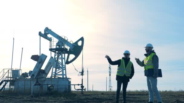 Deux hommes debout sur un champ sur un fond de tour de pétrole . — Video