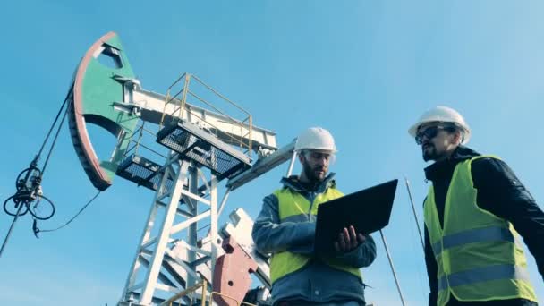 Personas que trabajan con una computadora portátil cerca de la torre de aceite, vista inferior . — Vídeos de Stock