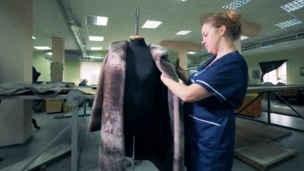 Dressmaker está cepillando un abrigo de piel que cuelga de un maniquí — Vídeos de Stock