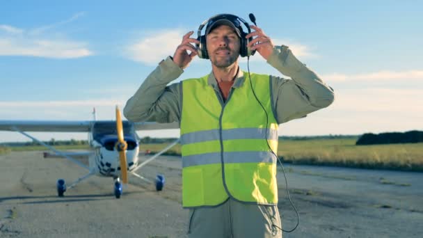 Мужчина-пилот носит наушники, стоящие на аэродроме, крупным планом . — стоковое видео