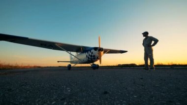 Pilot uçağa arıyorum. Bir pist üzerinde erkek pilot duruyor bir uçakta günbatımı bir arka plan üzerinde seyir.