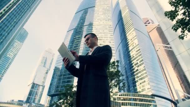 Podnikatel typy na tabletu na pozadí mrakodrapů, pohled zespodu. — Stock video