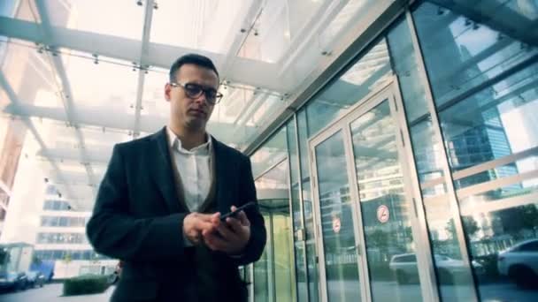 Corporate male manager talks on a mobile phone, walking on a street, close up. — Stock Video
