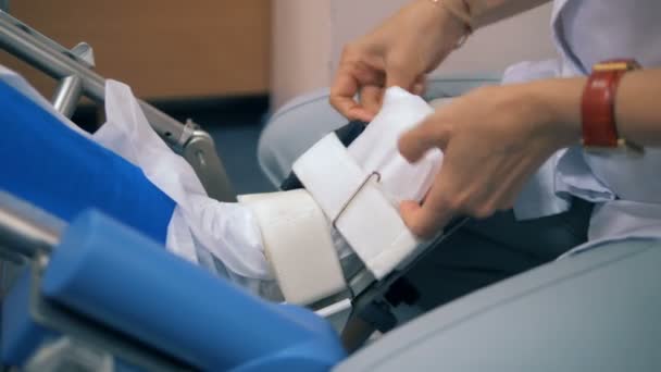 Νοσηλεύτρια ρυθμίζει ασθενείς πόδι σε μια μηχανή, εσωτερικη. — Αρχείο Βίντεο