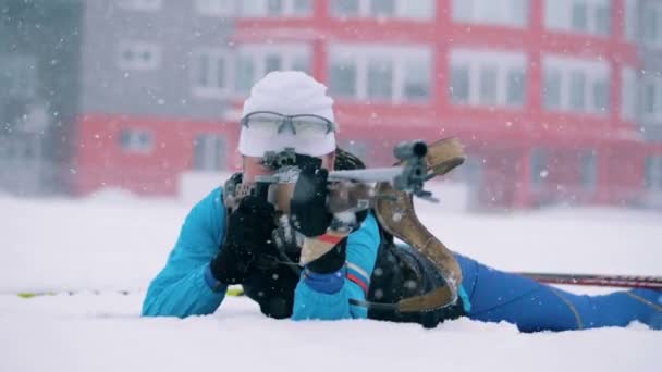 Vista frontal de una mujer biatleta disparando durante la nevada — Vídeos de Stock