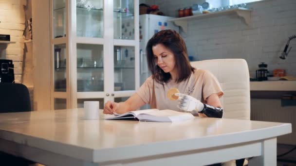 Mujer joven está leyendo un libro y sosteniendo una galleta con su mano biónica — Vídeo de stock