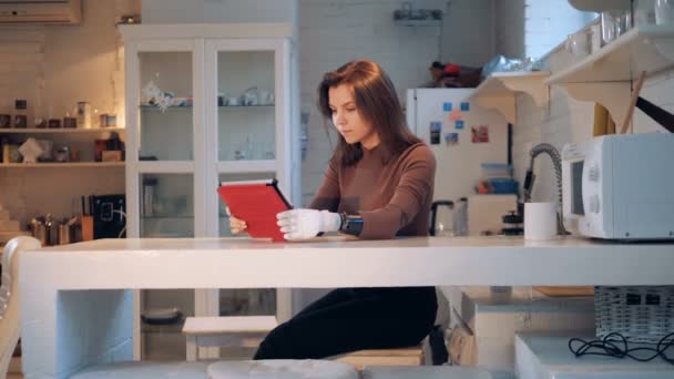 Una mujer con una mano protésica está trabajando con una tableta en una cocina — Vídeo de stock